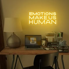 a laptop computer sitting on top of a desk under a neon sign that says emotions make us human