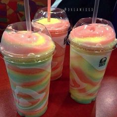 three drinks with straws sitting next to each other on a red counter top in front of a colorful background