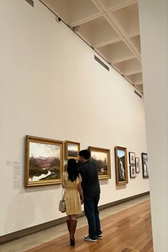 a man and woman standing in front of paintings on the wall at an art gallery