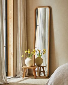 a mirror sitting next to a table with vases on it and flowers in front of it