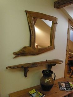 a wooden table with a mirror and vase on it next to a wall mounted shelf