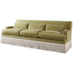 a green couch with fringe trim and pillows on the back, in front of a white background