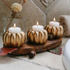 three gold pumpkin candles sitting on top of a wooden board next to a white sink