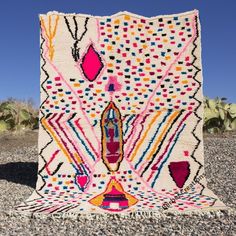 a multicolored area rug sitting on top of a gravel ground next to a cactus