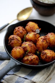 some food is in a black pan on a white tablecloth and silver spoons