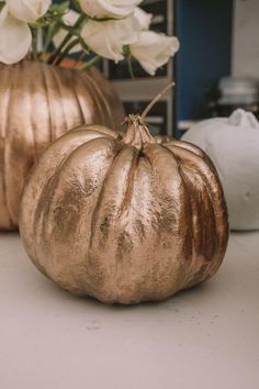 two gold pumpkins sitting on top of a table next to white flowers in vases