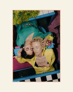 two women laying on top of each other in front of a green bag and flowers