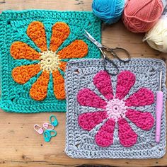 two crocheted squares with flowers on them and scissors next to each other in front of balls of yarn