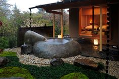 an outdoor hot tub surrounded by rocks and moss in front of a house with a patio