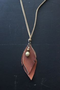 a brown leather leaf with a gold bead hanging from it's end on a cord