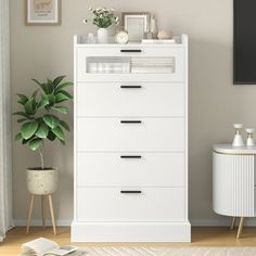 a white chest of drawers sitting next to a potted plant in a living room