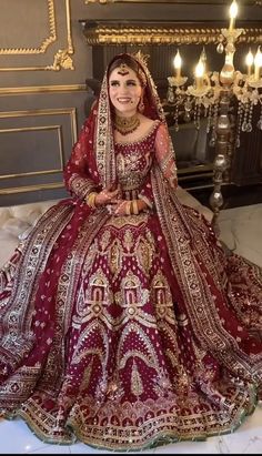 a woman in a red and gold wedding dress sitting on a bed with chandelier