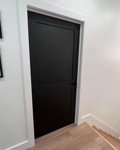 an empty room with a black door and wood flooring on the side of it