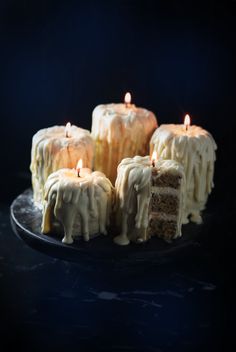 several slices of cake with white frosting on a black plate and lit candles in the middle