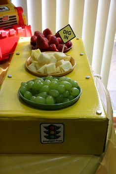 a yellow table topped with green grapes and strawberries next to a plate of fruit