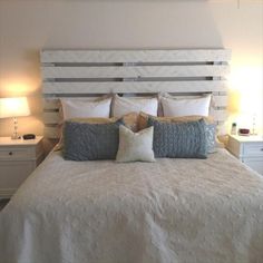 a white bed with two lamps on either side and one night stand in front of it