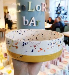 a person holding up a bowl with paint splattered on it in front of a table