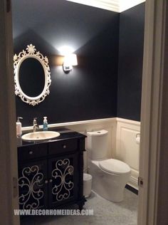 a white toilet sitting next to a black sink in a bathroom under a round mirror