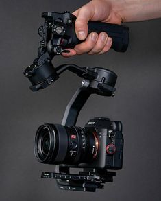 a hand holding a camera on top of a tripod with the lens attached to it