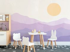 two white chairs sitting at a table in front of a wall with mountains painted on it