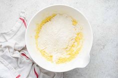 a white bowl filled with flour next to a red and white towel on top of a counter