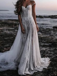 a woman standing on top of a rocky beach next to the ocean wearing a wedding dress