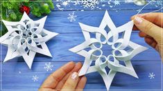 two snowflakes being made out of paper on a blue wooden surface with christmas decorations in the background