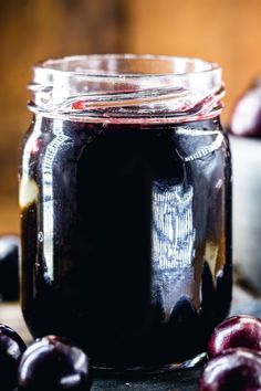 a glass jar filled with black liquid surrounded by cherries