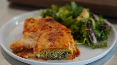 a white plate topped with lasagna next to a green leafy vegetable salad