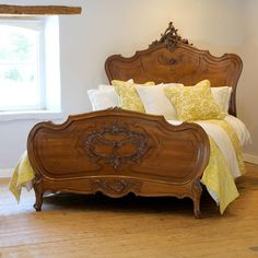 a wooden bed with yellow and white pillows on it's headboard, in front of a window