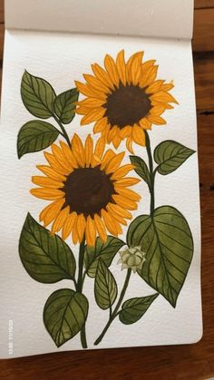 a painting of two sunflowers with green leaves on white paper, sitting on a wooden table