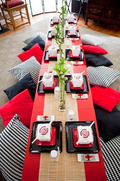 a long table set with black and red place mats, plates and flowers on it