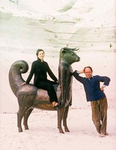 a man and woman standing next to a statue of a dog on top of a horse