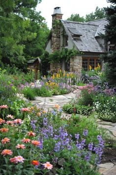 a stone house surrounded by colorful flowers and greenery in the foreground is a path leading to it