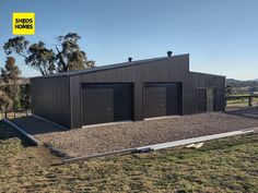 two garages in the middle of a field with mountains in the background and trees on either side