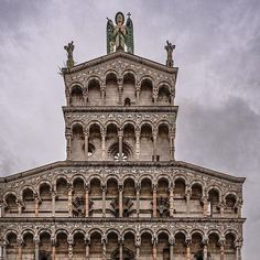 an old building with statues on the top and below it's roof, against a cloudy sky