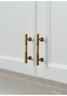 two brass handles on the front door of a white cabinet