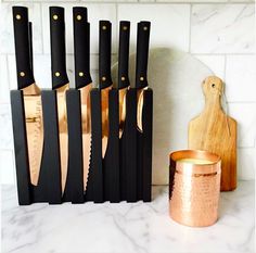 black and gold knives are lined up next to a wooden cutting board on a marble counter