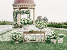 an outdoor ceremony setup with white flowers and greenery on the grass, in front of a gazebo