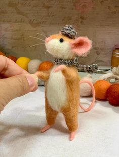 a hand is holding a needle - felt mouse in the shape of a rat with a hat on it's head