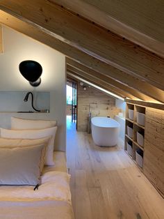 an attic bedroom with white bedding and wooden walls, along with a bathtub in the corner