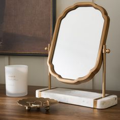 a mirror sitting on top of a wooden table next to a candle and a vase