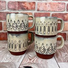 two coffee mugs sitting next to each other on top of a wooden table near a brick wall