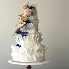 a three tiered white cake with flowers on top and blue ribbon around the edges