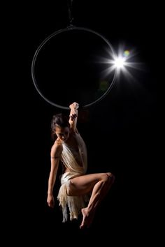 a woman in white dress doing aerial acrobatics on black background with light