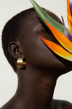 a woman with an orange flower on her head and gold hoop earrings in front of her face