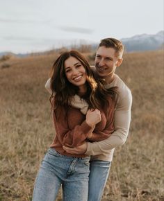 a man and woman are standing together in the grass with their arms around each other