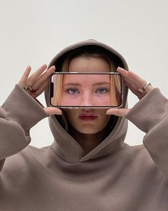 a woman in a hoodie holding up her cell phone to take a selfie