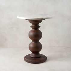 a white marble topped table on a wooden base with an iron ring at the top