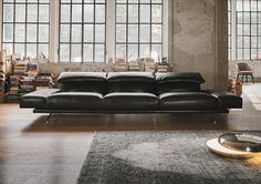 a black leather couch sitting on top of a wooden floor in front of two large windows